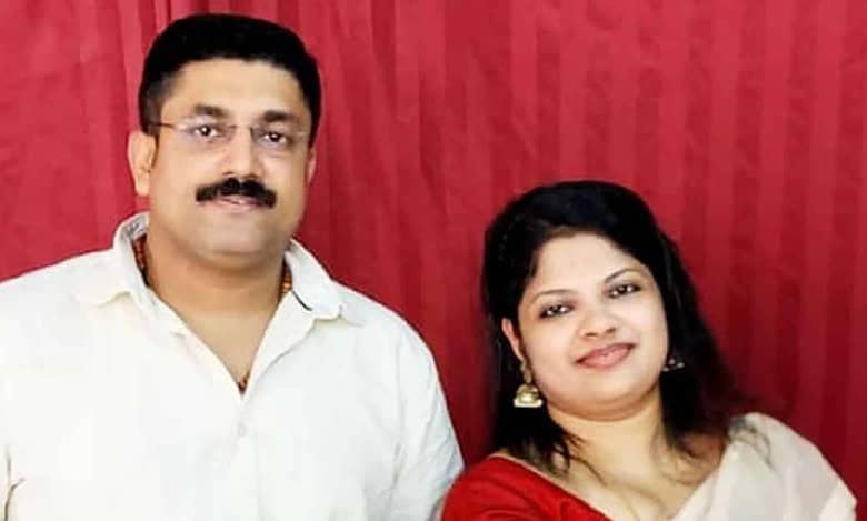 Suraj and Binsi, an Indian couple from Kerala, smiling together in a posed photo against a red curtain backdrop.