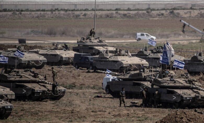 Israeli tanks with national flags positioned near Gaza border during ongoing military operations.