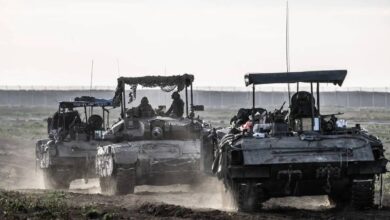 Israeli army tanks and armoured vehicles advancing through a dusty field near Gaza border during a military operation.