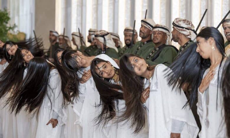 Emirati girls in white gowns perform the traditional Khaleeji dance by rhythmically flipping their hair in unison, as part of a ceremonial welcome for U.S. President Donald Trump in Abu Dhabi. Men in traditional dress stand behind them holding swords.