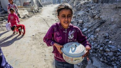 A Palestinian girl carries a food container while walking through a rubble-strewn street in Khan Younis, Gaza, following humanitarian aid distribution on Sunday, 18 May.