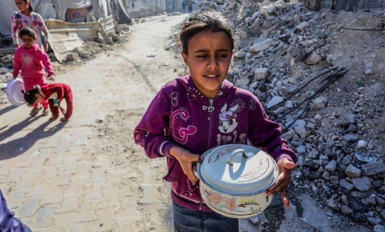 A Palestinian girl carries a food container while walking through a rubble-strewn street in Khan Younis, Gaza, following humanitarian aid distribution on Sunday, 18 May.