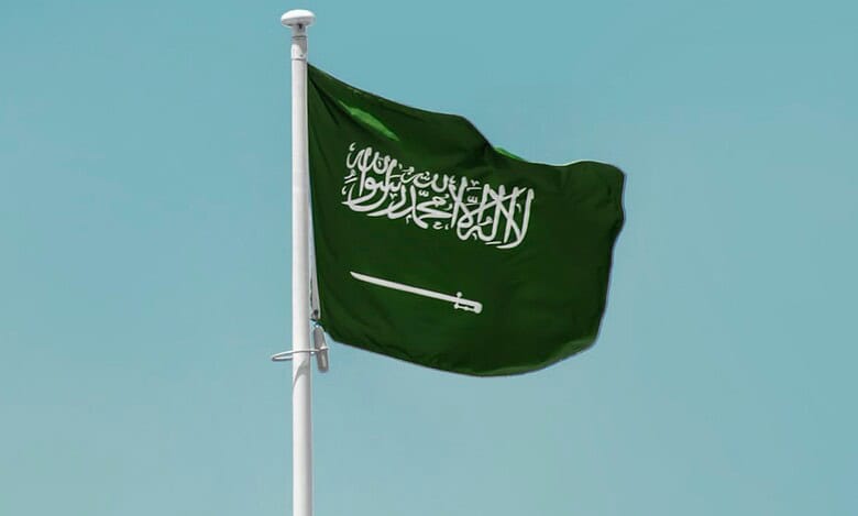 Saudi Arabian national flag waving on a clear blue sky background.