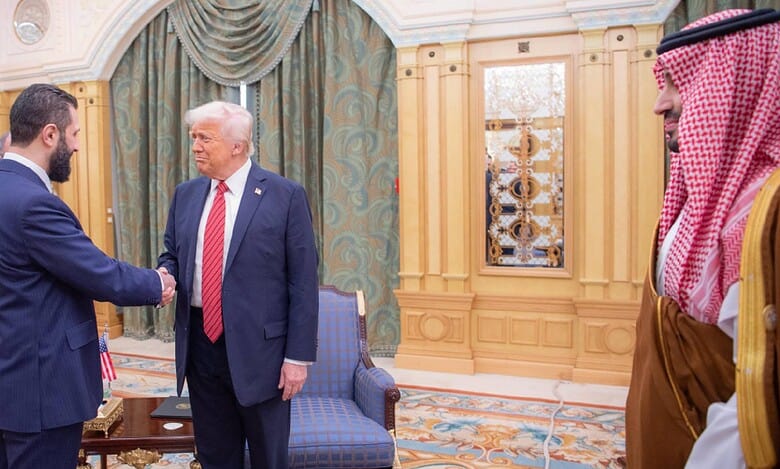 US President Donald Trump shakes hands with the interim Syrian President during a formal meeting in Saudi Arabia, as a Saudi Crown Prince observes from the side.