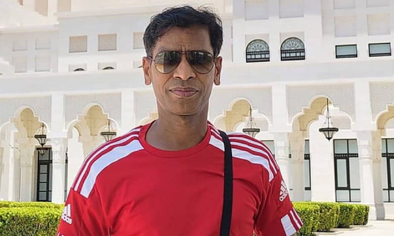 Venkata Giribabu Vulla, Qatar-based Indian Big Ticket winner, stands in front of white building in red Adidas shirt and sunglasses.