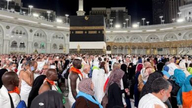 A large gathering of international pilgrims dressed in white Ihram and traditional attire at Makkah’s Grand Mosque, with the Kaaba in the background, during the night ahead of Haj 2025.