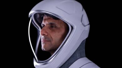 The image of a Indian astronaut Shubhanshu Shukla in a white space helmet, facing left, against a black background.