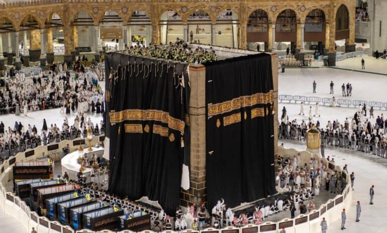 Workers replace the Kiswah (cloth covering) of the Kaaba at the Grand Mosque in Makkah, surrounded by pilgrims and security personnel.