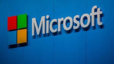 The Microsoft logo displayed on a blue wall, featuring the company name in white letters next to the red, green, blue, and yellow square icon.