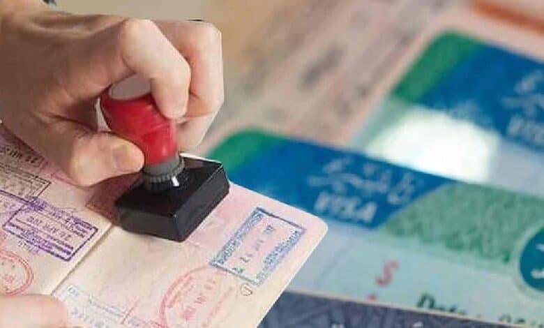A close-up of a hand stamping a passport, with Saudi Arabian visa documents visible in the background.