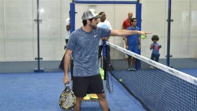 Sheikh Hamdan bin Mohammed bin Rashid Al Maktoum, Crown Prince of Dubai, playing padel on an indoor court, holding a paddle, with other players and a child in the background.