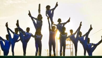 Young performers in blue outfits display a coordinated yoga formation at sunrise during International Day of Yoga celebrations.