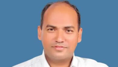 The image of of Aju Paul, an Indian man wearing a white shirt, posing against a plain blue background.