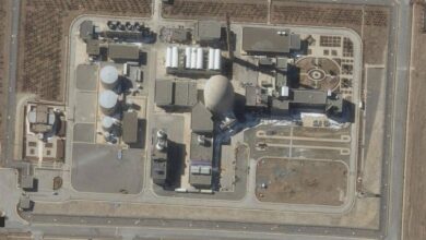 A satellite image shows the Arak heavy water reactor in Iran. The facility includes large cylindrical tanks, a domed reactor building, and various support structures, surrounded by access roads and sparse vegetation.