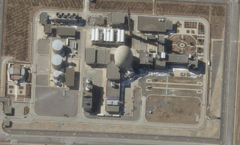 A satellite image shows the Arak heavy water reactor in Iran. The facility includes large cylindrical tanks, a domed reactor building, and various support structures, surrounded by access roads and sparse vegetation.