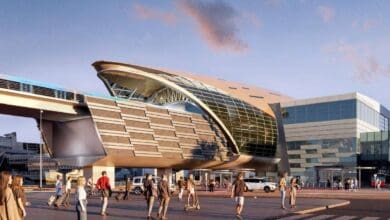 A futuristic architectural design of the Burj Khalifa-Dubai Mall Metro Station expansion in Dubai, featuring a sleek glass and steel structure with pedestrians walking in the foreground during sunset.