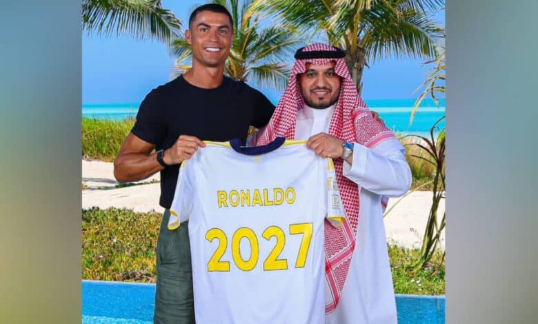 The image of Cristiano Ronaldo stands beside an Al Nassr official on a tropical beach, holding a football jersey with his name and "2027" printed on the back, celebrating his contract extension.