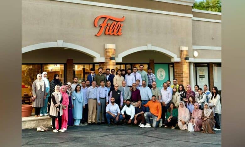 A large group of men and women pose together outside FiLLi Cafe in Villa Park, Illinois, during the DAANA mentorship event. The café's exterior features the orange FiLLi sign above, with attendees dressed in a mix of formal and semi-formal attire.