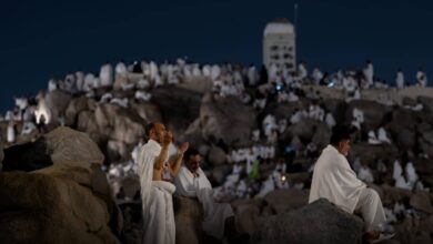 Pilgrims in ihram garments pray and reflect on Mount Arafat under the night sky during Haj 2025, surrounded by crowds on the rocky slope.