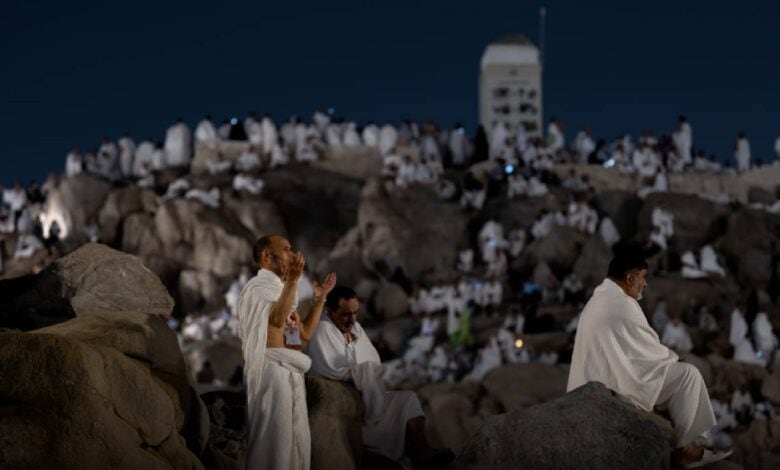 Pilgrims in ihram garments pray and reflect on Mount Arafat under the night sky during Haj 2025, surrounded by crowds on the rocky slope.