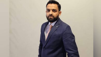 The image of a Indian banker Mustafa Mohammed wearing a navy blue suit and peach-striped tie poses confidently against a plain beige background.