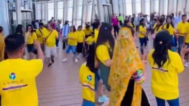The image of a group of Indian tourists wearing matching yellow T-shirts dance Garba on the viewing deck of the Burj Khalifa in Dubai, as other visitors look on.