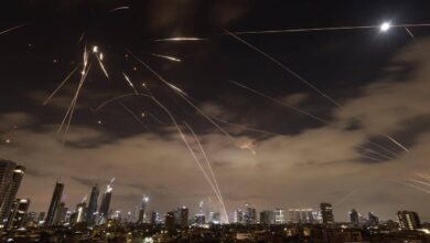 The image of a Israeli air defence systems intercepting Iranian missiles over Tel Aviv at night, with bright trails of interceptor rockets lighting up the sky above the city skyline.