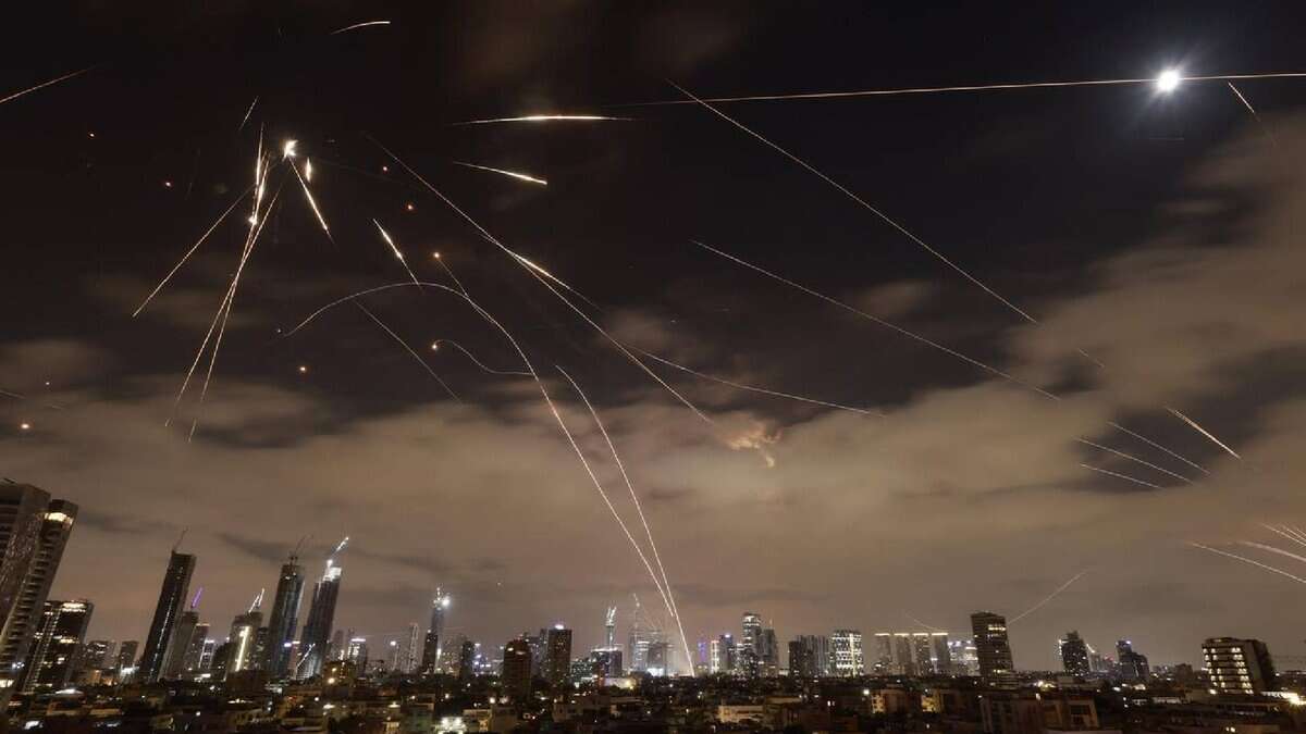 The image of a Israeli air defence systems intercepting Iranian missiles over Tel Aviv at night, with bright trails of interceptor rockets lighting up the sky above the city skyline.