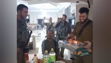 The image of a Israeli soldiers in uniform celebrate a birthday inside a Palestinian home, with one holding a cake and others clapping and filming the scene.