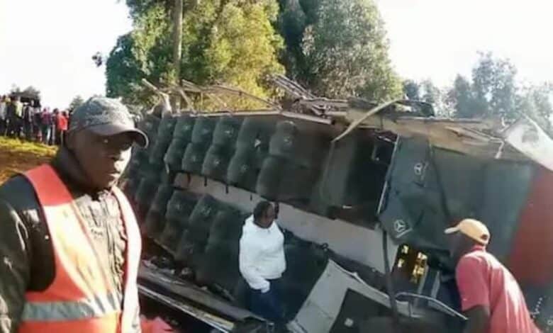 Crowd gathers around an overturned tour bus in Kenya after a fatal accident; emergency responders and bystanders are seen at the scene.