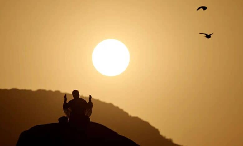 Pilgrim praying at dawn on Mount Arafat during Haj pilgrimage in Saudi Arabia, with sunrise in the background.