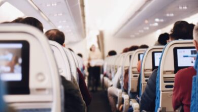The image of a Interior of an aeroplane cabin showing seated passengers and a flight attendant standing in the aisle.