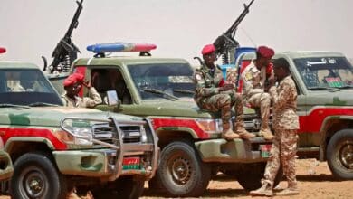 The image of Sudanese paramilitary Rapid Support Forces (RSF) soldiers in uniform sit and stand around armed pickup trucks in a desert area, equipped with mounted machine guns.