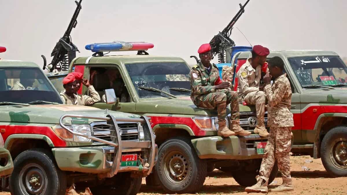 The image of Sudanese paramilitary Rapid Support Forces (RSF) soldiers in uniform sit and stand around armed pickup trucks in a desert area, equipped with mounted machine guns.