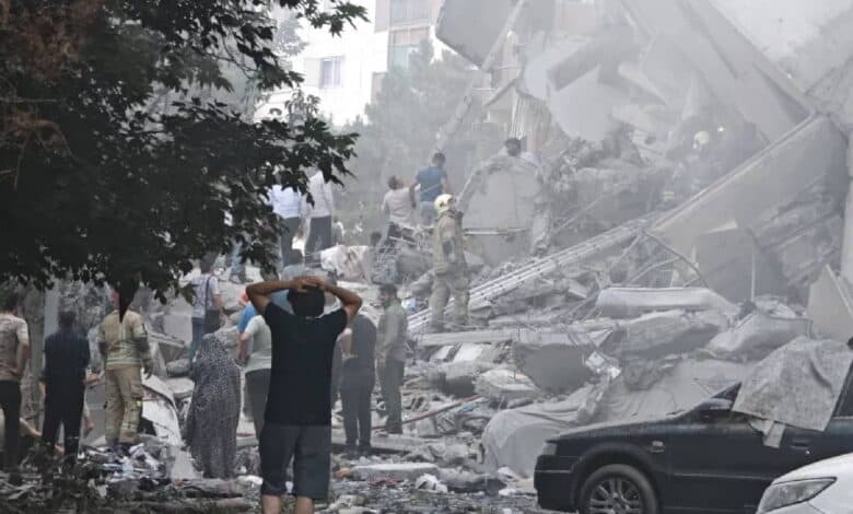 People search through rubble and damaged vehicles after a building collapsed in Tehran, Iran. The area is filled with dust and debris as rescuers and civilians gather at the scene of destruction caused by airstrikes.