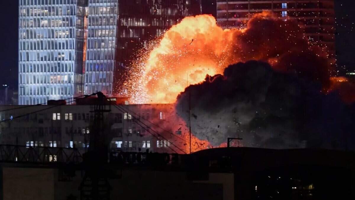 The image of a massive explosion with bright orange flames and thick black smoke erupts in front of modern high-rise buildings at night in Tel Aviv, reportedly during Iran's missile attacks on Israel.