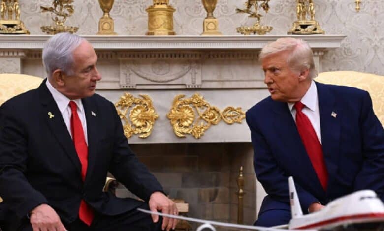 US President Donald Trump (right) and Israeli Prime Minister Benjamin Netanyahu (left) sit facing each other in a formal setting, likely the Oval Office. Both are wearing dark suits with red ties. A model airplane is placed on the table between them. Behind them is an ornate fireplace decorated with gold vases and intricate embellishments, highlighting the room's grandeur.