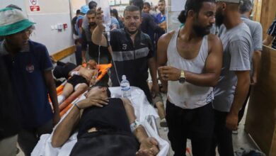 Palestinians wounded while returning from a Gaza Humanitarian Foundation aid centre lie on stretchers and are treated by others inside Nasser Hospital in Khan Younis. The crowded emergency room shows visible signs of distress, with injured individuals receiving IV fluids and first aid.