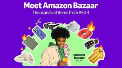 A promotional image for Amazon Bazaar featuring a smiling person with curly hair holding a smartphone, surrounded by various products including a phone case, sunglasses, slippers, a belt, a shirt, a travel pillow, and a wallet, with flames and heart emojis. The background is purple, and the text reads "Meet Amazon Bazaar Thousands of items from Dirham 4" with the Amazon Bazaar logo.