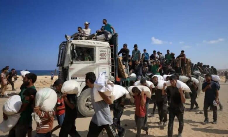 Palestinians carry sacks of aid as others ride atop a truck in Beit Lahia, northern Gaza, amid ongoing humanitarian crisis.