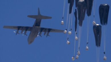 A military airplane in flight dropping humanitarian aid packages with parachutes over a clear blue sky, viewed from the northern Gaza Strip.