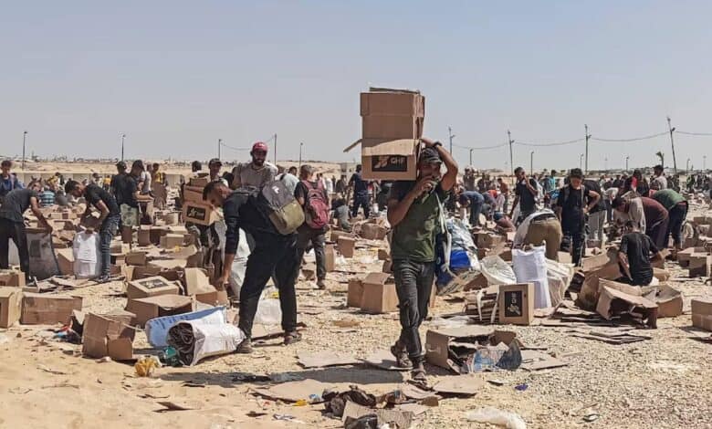 The image of people gather at a Gaza aid distribution site, collecting boxes and supplies scattered across a dusty, open area under the sun.