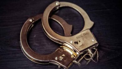 The image of a pair of metal handcuffs resting on a dark wooden surface.