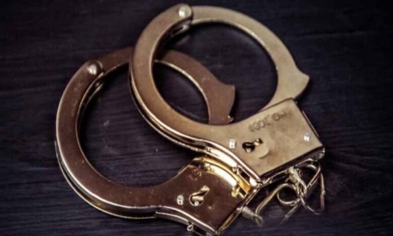 The image of a pair of metal handcuffs resting on a dark wooden surface.