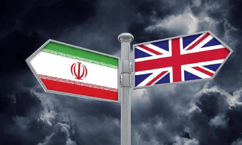 A signpost with two directional arrows, one displaying the Iranian flag on the left and the other the United Kingdom flag on the right, set against a dark, stormy cloud background.