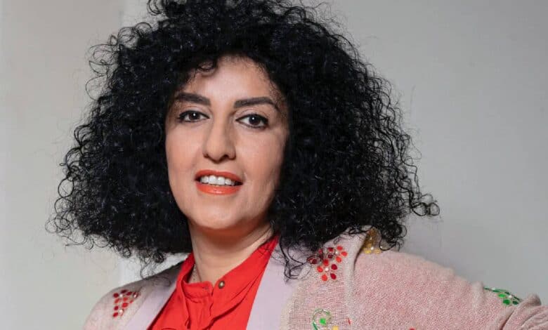 Narges Mohammadi, Iranian human rights activist and Nobel Peace Prize laureate, poses in a red blouse and embroidered jacket, smiling slightly with her curly black hair framing her face.