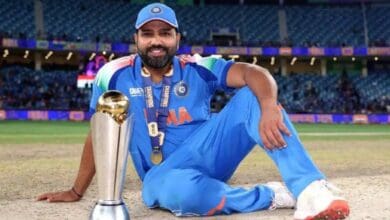 The image of a Rohit Sharma in Indian cricket jersey sitting on the field with a trophy, smiling after a championship win.
