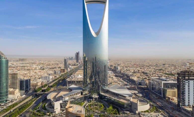Aerial view of the Kingdom Centre Tower, a modern skyscraper with a distinctive glass design and skybridge, standing prominently in Riyadh's urban skyline, surrounded by contemporary buildings in the desert landscape of Saudi Arabia.