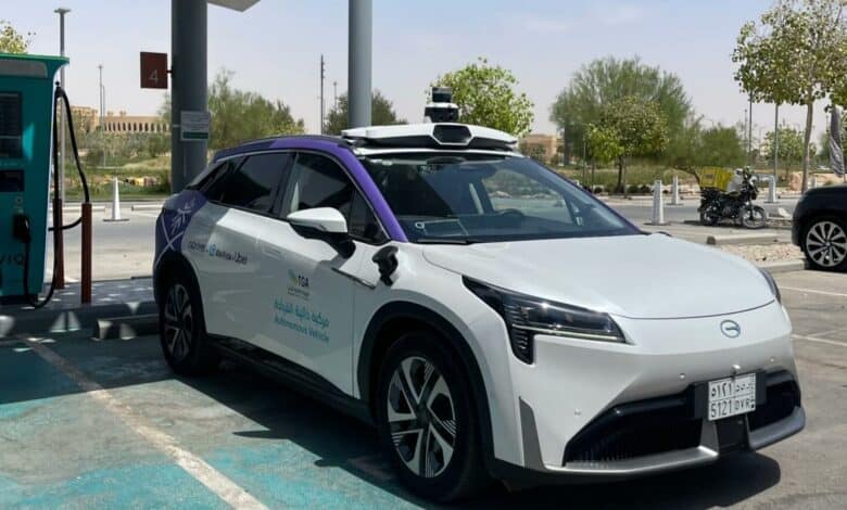 A self-driving electric taxi with TGA and Uber logos parked at a charging station in Riyadh during Saudi Arabia’s pilot launch.