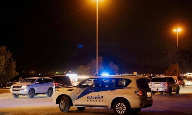 The image of a Sharjah Police patrol vehicle with flashing lights parked at night, surrounded by other cars under streetlights.